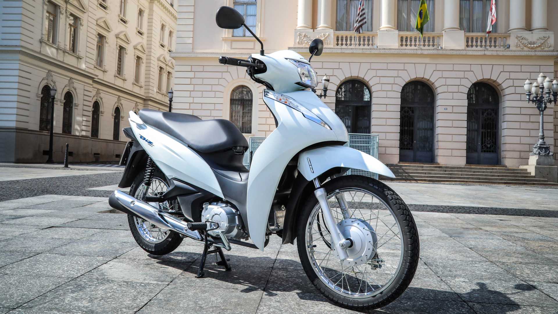 Honda Biz 110i 2020 branca estacionada em frente a uma construção antiga