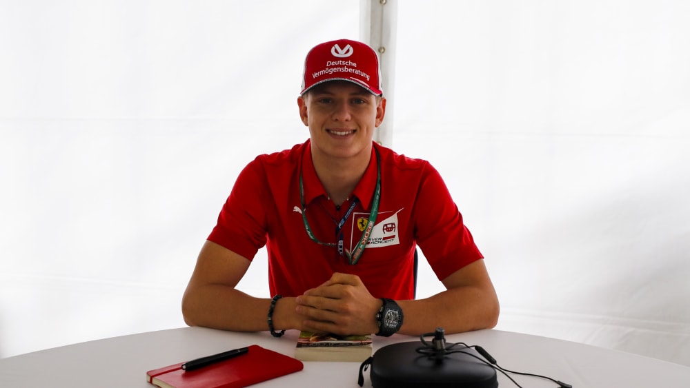 Mick Schumacher, filho de Michael Schumacher, posa para foto com boné vermelhor e camisa vermelha