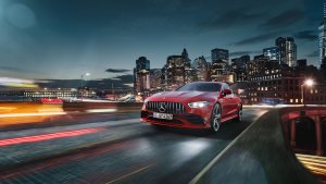 Mercedes-AMG GT 43 vermelho em movimento com faróis acesos em uma pnte com cidade iluminada e grandes arranha-céus ao fundo