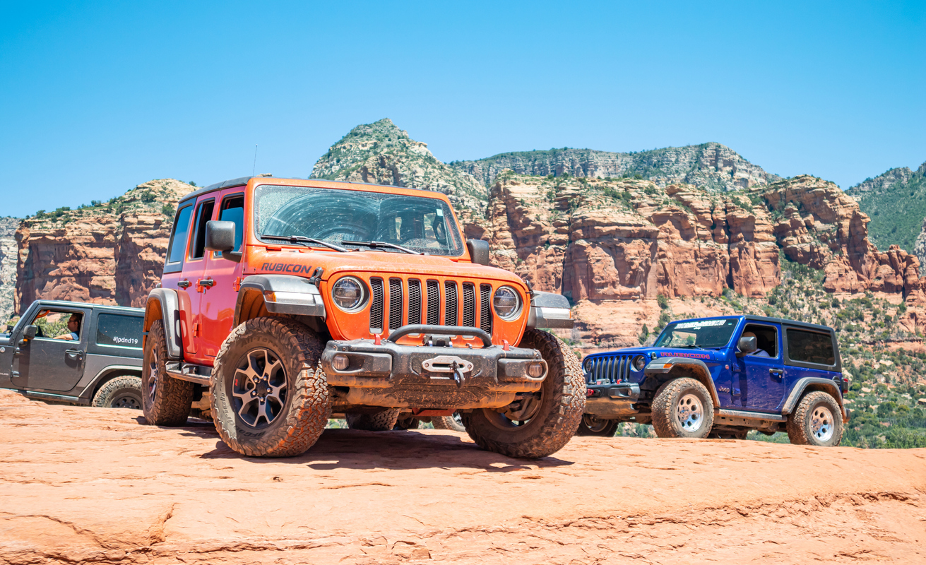 Jeeps colorido, carros off-road, parados em estrada de terra, com céu azul e paisagem natural ao fundo