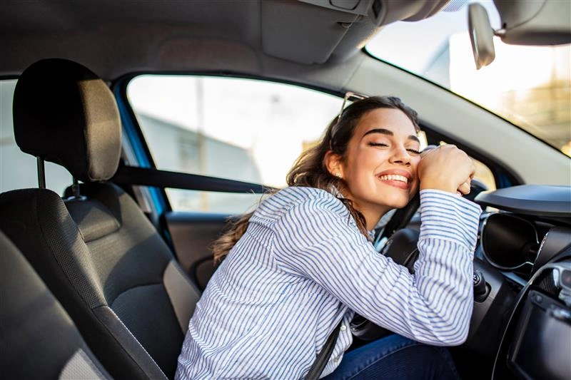Jovem feliz após escolher o primeiro carro no Feirão e Black Feirão Webmotors e fazer a compra abraçando o volante